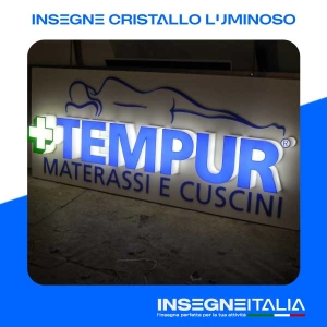 Insegna in Cristallo Luminoso della scritta TEMPUR MATERASSI E CUSCINI, con logo di una croce in rilievo molto marcato e la silhouette di una donna sdraiata sulla scritta, illuminate da una luce delicata interna